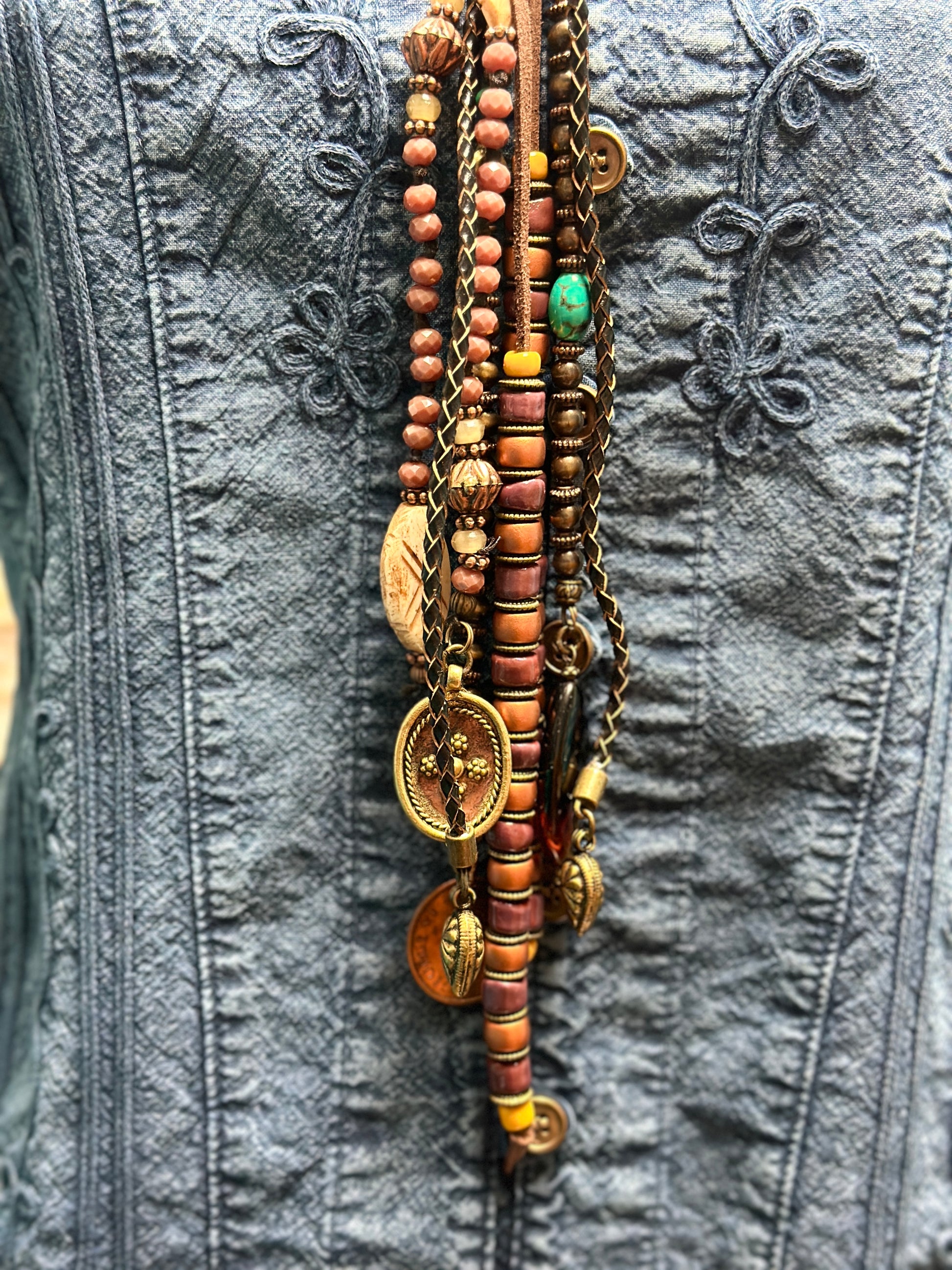 Necklace with beads and charms on denim jacket.