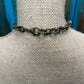 Close-up of a bronze-colored chain necklace clasp on a burlap-covered neck form.
