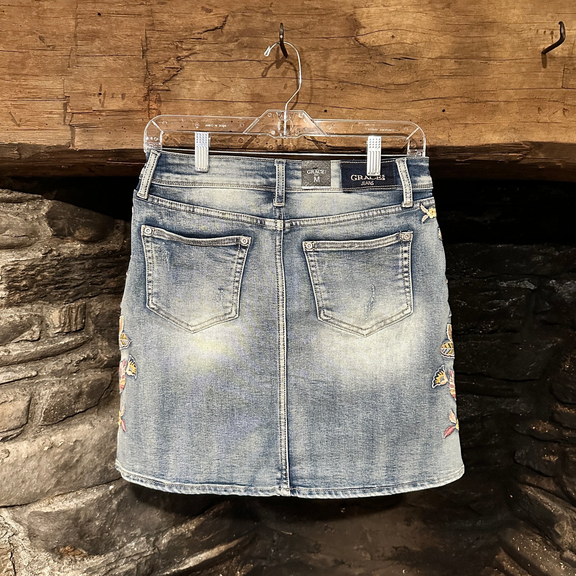Denim skirt with floral embroidery hanging on a hanger.