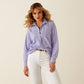 Woman wearing a warm-toned blue shirt and white pants