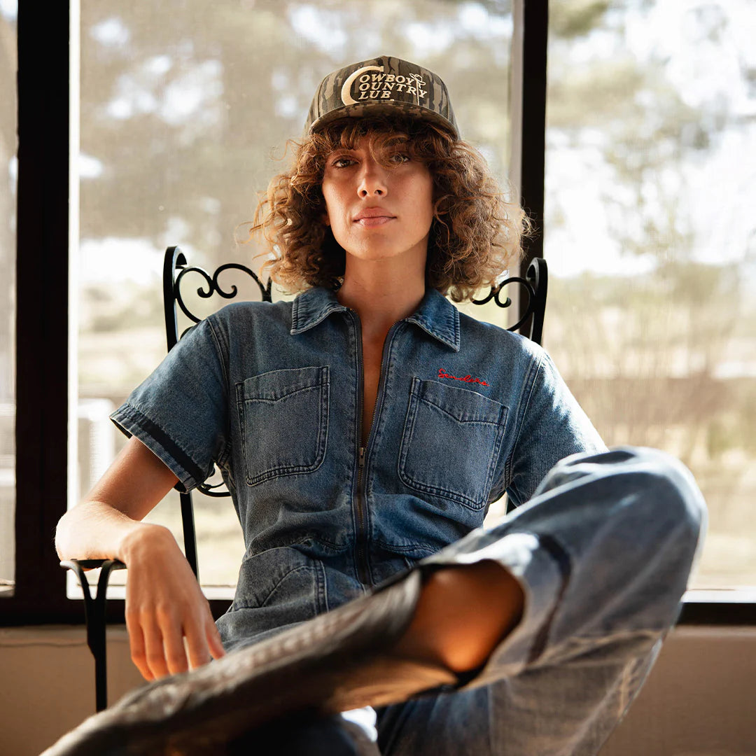 The Dolly Jumpsuit in Medium Indigo, model wearing cap.