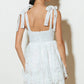 Woman wearing a white lace dress with bow straps.