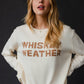 Woman wearing a cream sweater with Whiskey Weather text.
