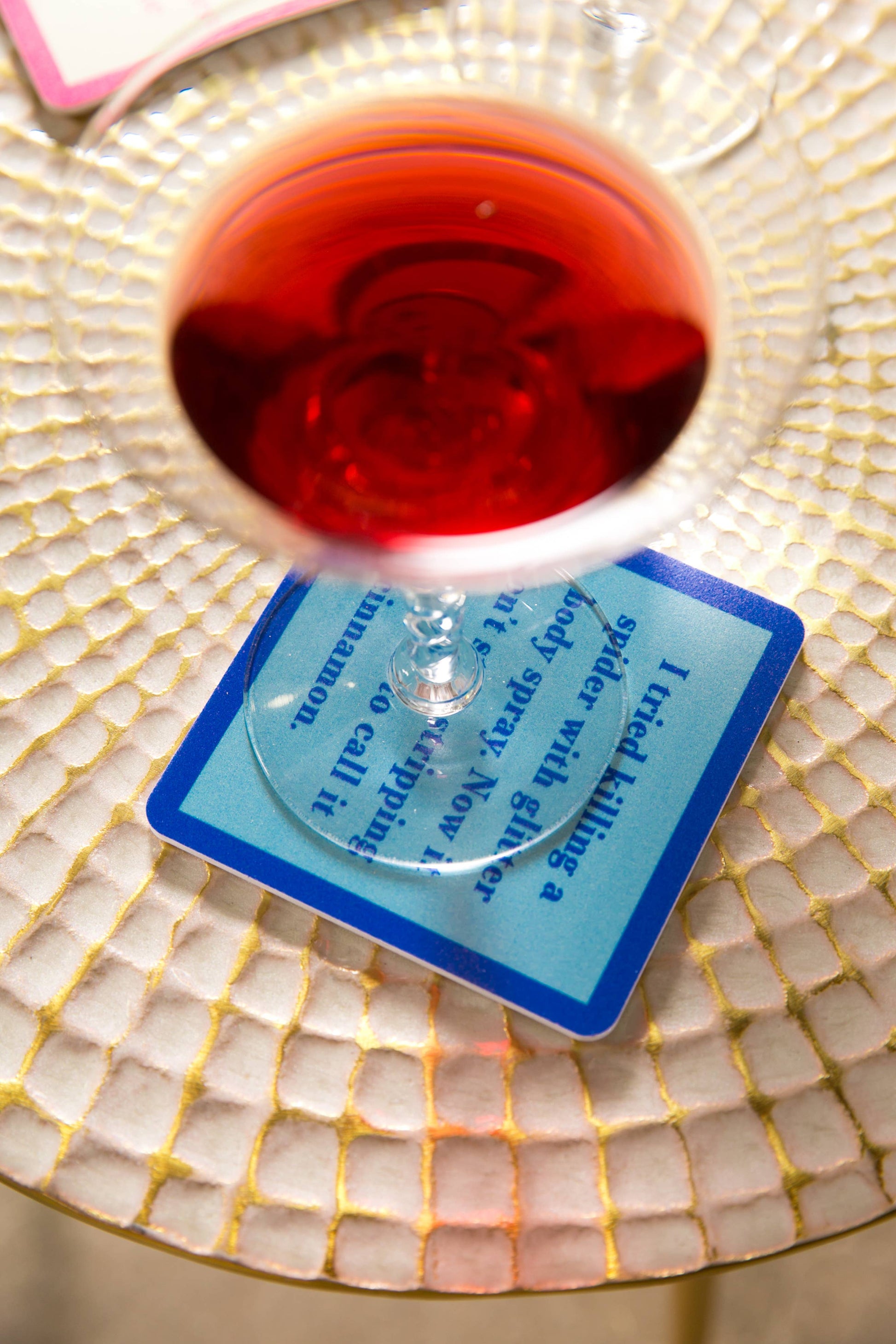 Red drink in glass on coaster with text.