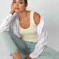 Woman in tank top, jeans, and shirt, seated.