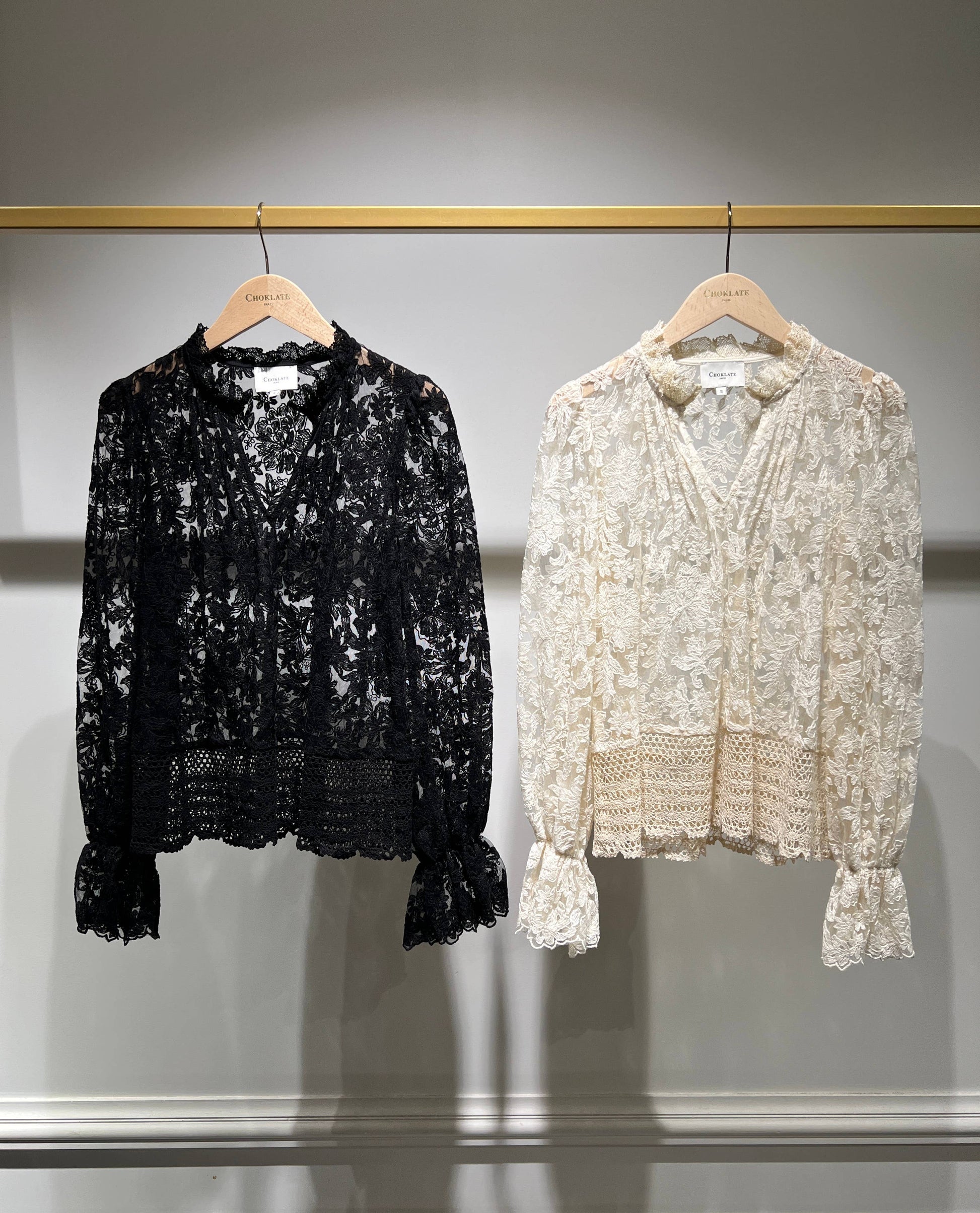 Two lace blouses hanging on a rack.