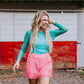 Woman in turquoise top and pink fringed shorts.