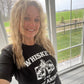 Woman in black t-shirt smiling near a window.