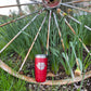 Red tumbler in front of a rusty wagon wheel and plants.