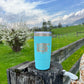 Turquoise tumbler on a wooden fence with a landscape background.