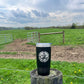 Black tumbler on a wooden post in a field.